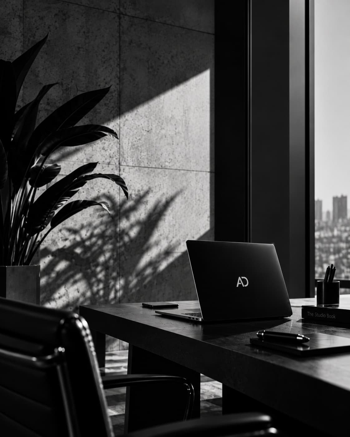 Escritório em preto e branco, com luz natural e um notebook com a marca AD